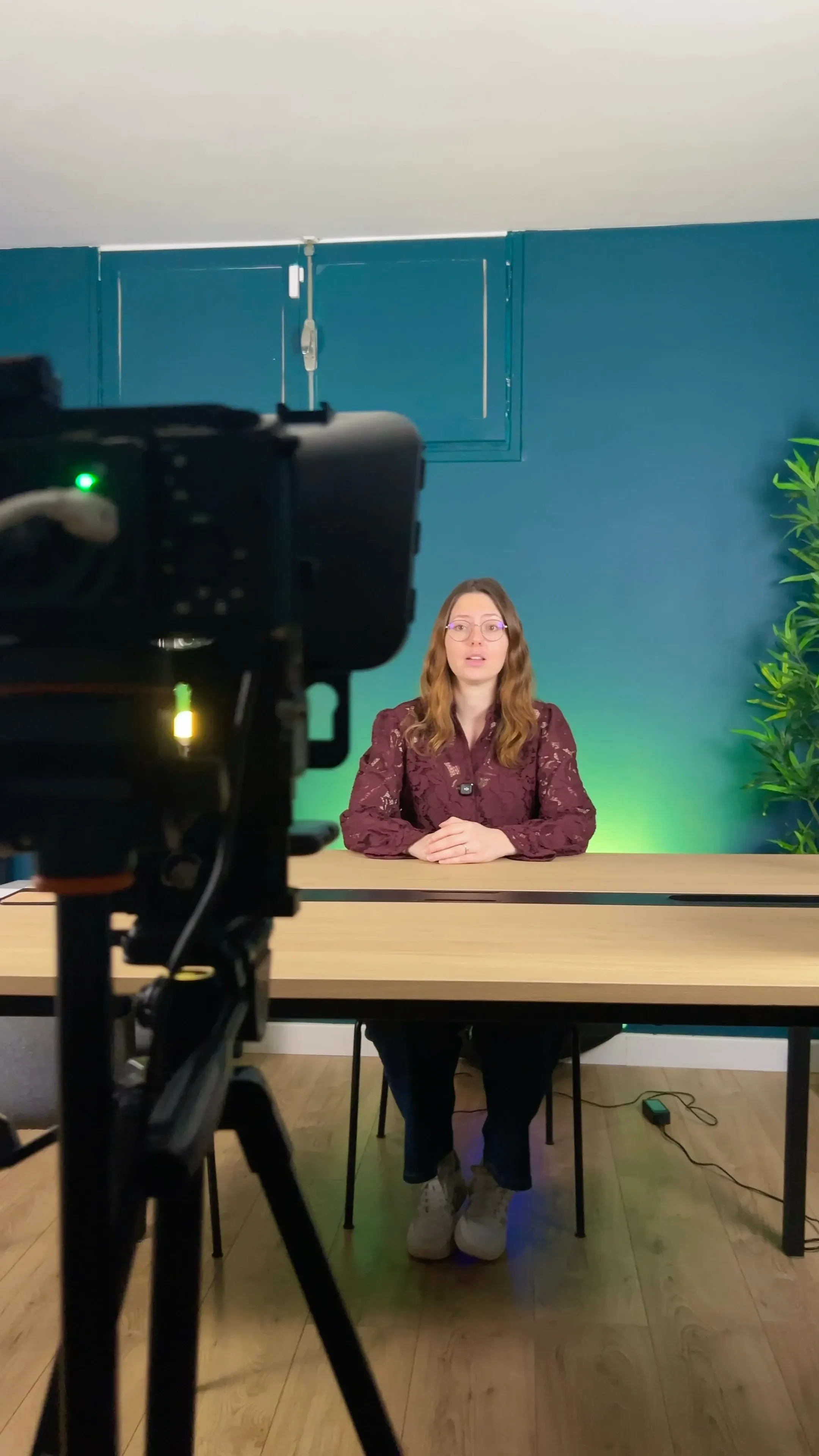 Une intervenante parle face caméra, assise à une table dans le studio Welprod, une caméra au premier plan.